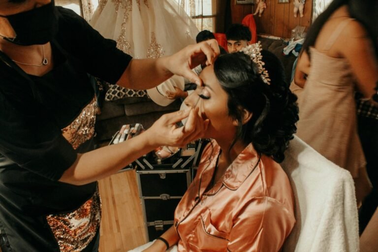 A bride in peach robe getting her makeup done by an artist before her wedding celebration.