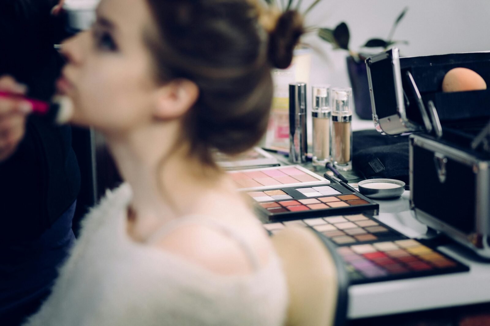 A woman receiving professional makeup in a studio with various cosmetics in focus.