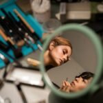 Makeup artist applying creative makeup, viewed through a mirror reflection.