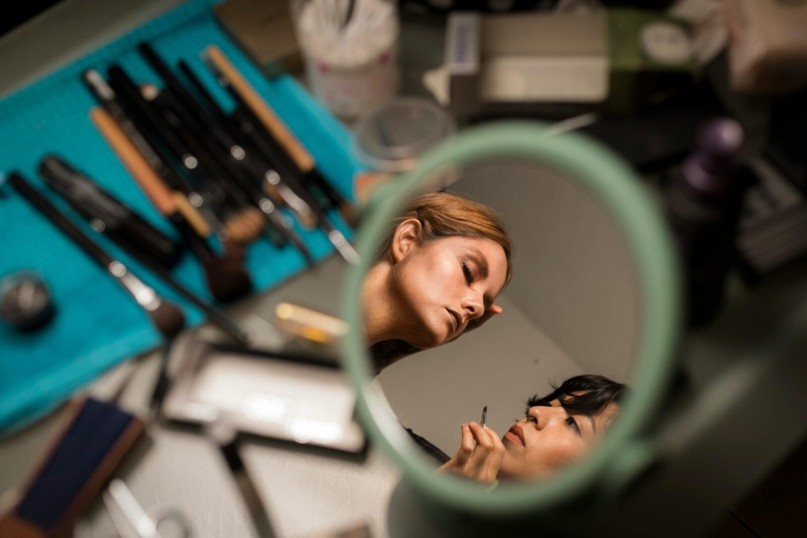 Makeup artist applying creative makeup, viewed through a mirror reflection.